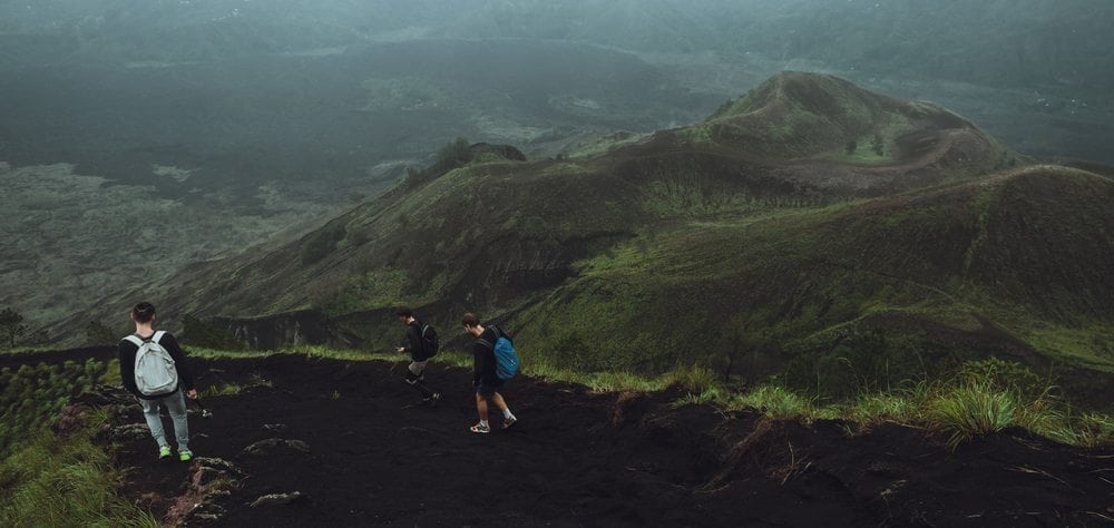 3 Men walk along the hill with backpacks and with white clouds a