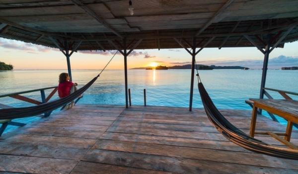 Togean Islands Sunrise, Togian Islands travel destination, Sulawesi, Indonesia. Woman looking at view on hammock, transparent turquoise water with scattered islets.